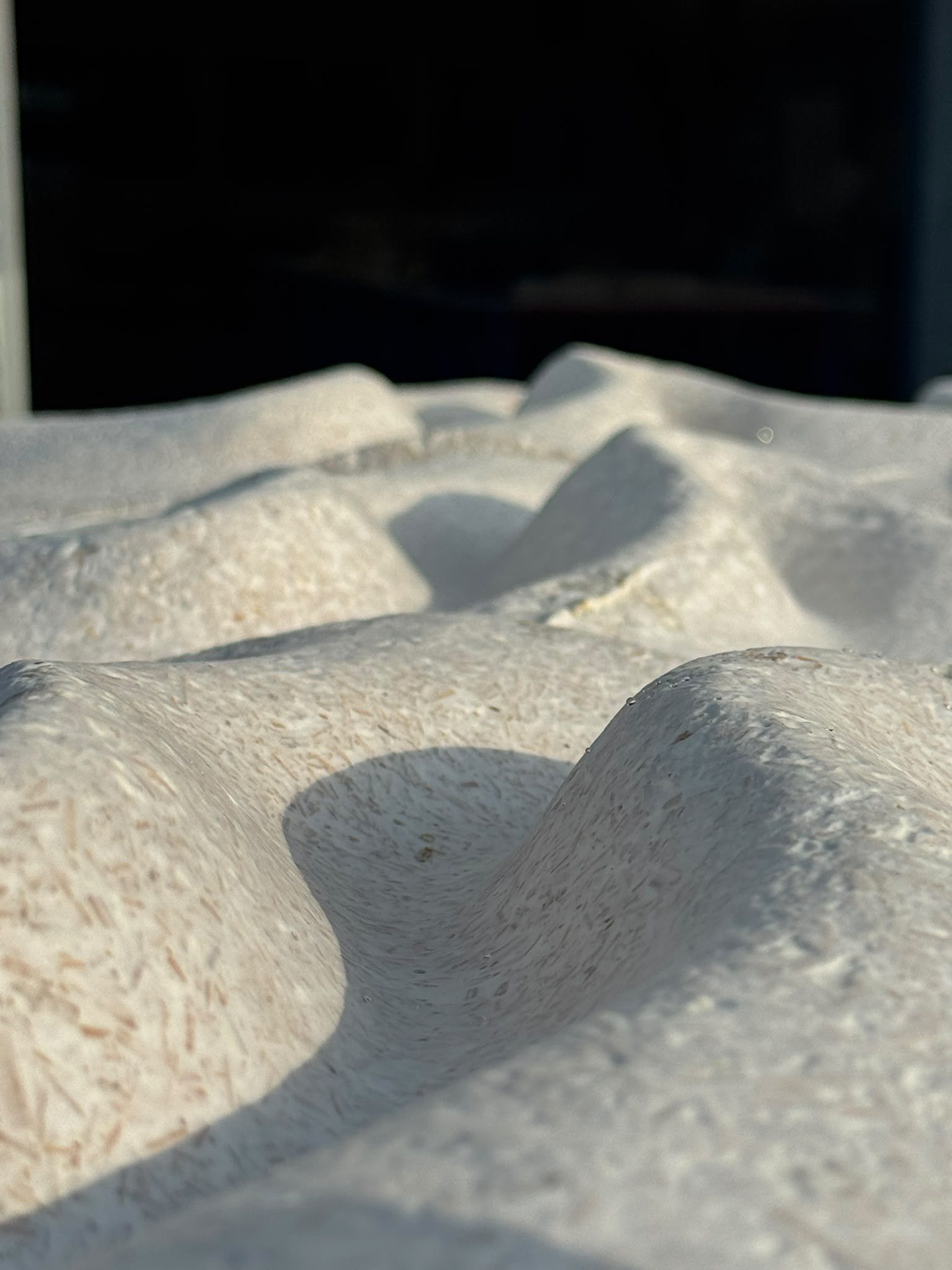 Low sunlight across the grown relief of FOLD panels, showing the palm-fibre texture