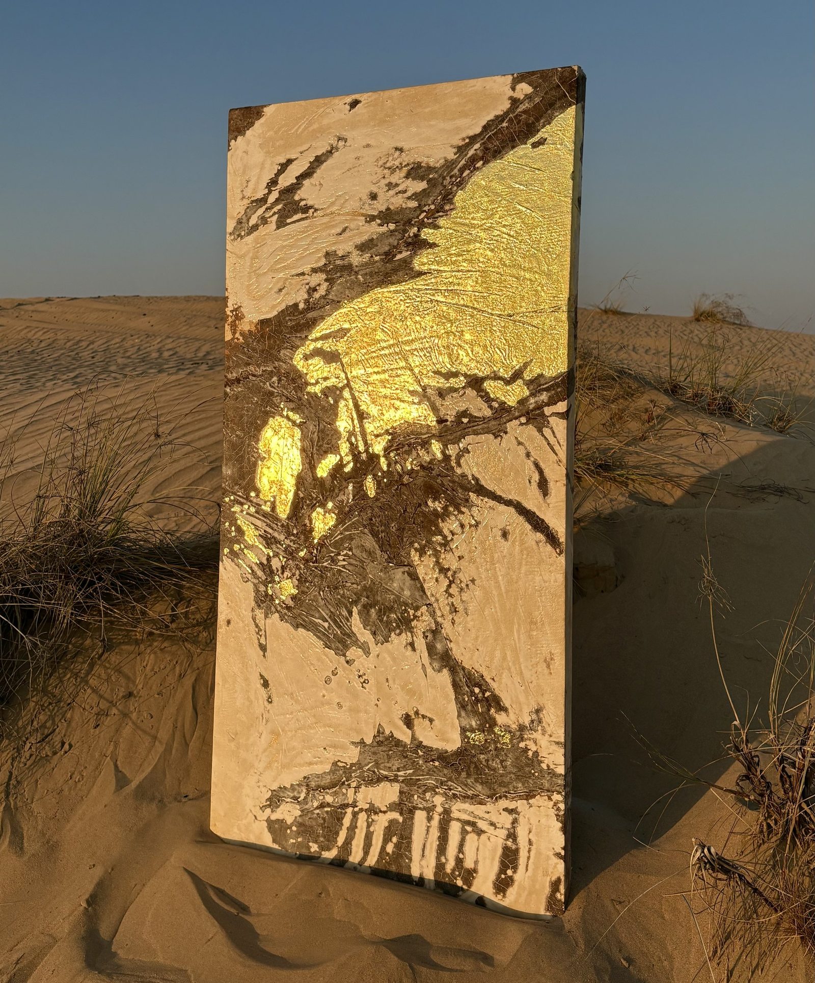 Aurum standing on a desert dune at sunset, gold catching the low light